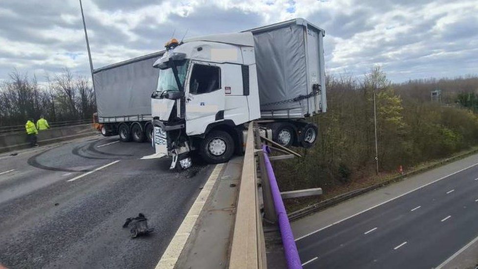 A truck in Britain crashed into the guardrail and hung halfway on a 24-meter-high bridge. The driver successfully escaped.